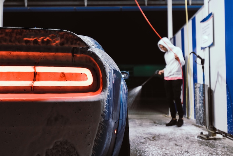 Man using a pressure washer wand on a car at a self-serve bay